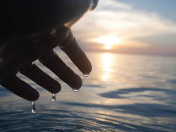 Midsection of person holding sea against sky during sunset