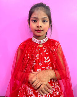 Portrait of young woman standing against pink background