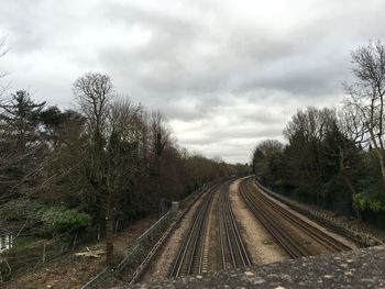 Road passing through field against cloudy sky