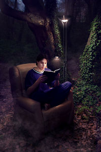 Young woman using phone while sitting on bench at night
