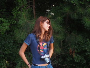 Teenage girl carrying camera while standing against trees