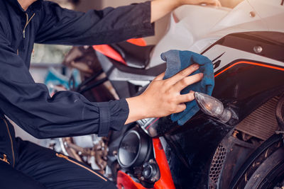 Midsection of mechanic wiping motorcycle in garage