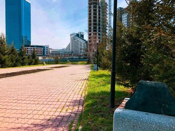 Footpath by buildings in city against sky