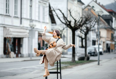 Playful woman balancing on a high chair on a city street