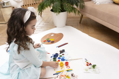 Cute curly girl with a paint palette, gouache paints, brushes and pencils. little painting artist.