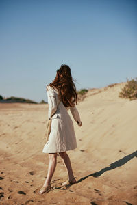 Rear view of woman standing at beach against clear sky