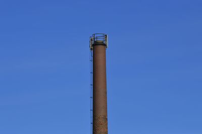 Low angle view of smoke stacks against clear blue sky