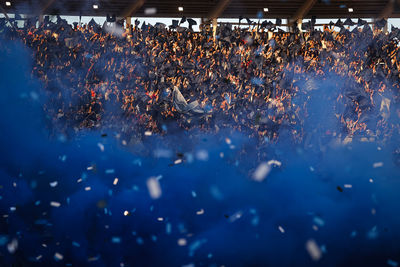Argentine soccer fans welcome their team with flags, confetti and blue smoke inside a stadium 