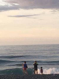 People walking on beach against sky during sunset