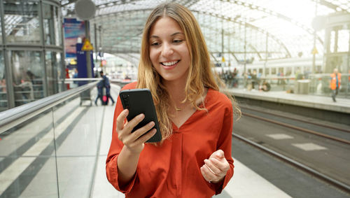 Young smiling woman holding mobile phone on sun flare platform station. 