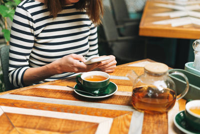 Young brunette woman in casual clothes using social media on mobile phone sitting at cafe