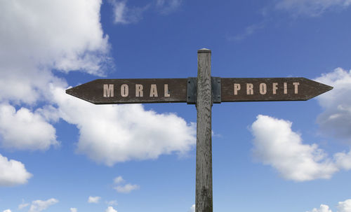 Low angle view of sign on wooden post against sky