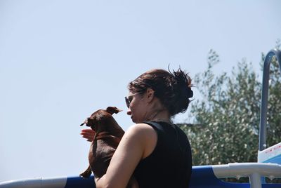 Low angle view of woman holding dog against clear sky