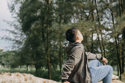 Side view of young man sitting in forest