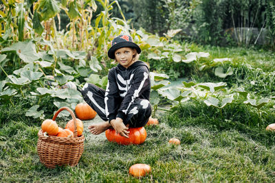 A girl in a skeleton carnival costume is sitting on a large pumpkin in the garden. halloween,