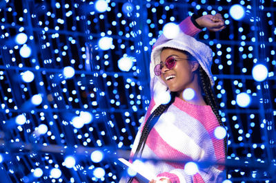 Joyful woman of color with a white beanie braided hairstyle and pink glasses enjoying the christmas