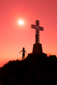 Silhouette person standing on cross against sky during sunset