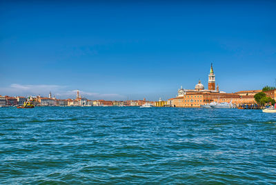 View of buildings at waterfront against blue sky