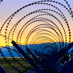 Close-up of metal fence against sky during sunset