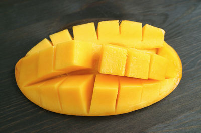 Closeup of fresh ripe juicy mango in half with crosswise cut on black wooden backdrop