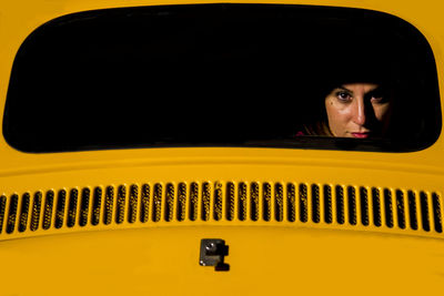 Portrait of young woman seen from yellow car rear windshield