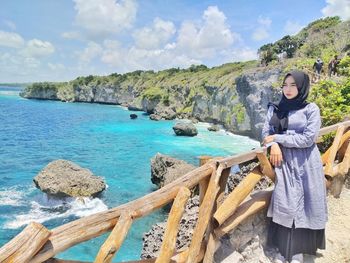 Young woman standing on rock by sea against sky