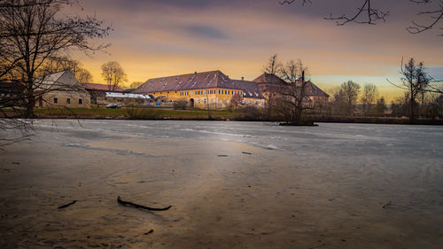 Built structure by bare trees against sky during sunset