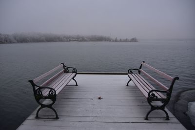 Bench by lake against sky