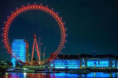 Illuminated millennium wheel and buildings against sky at night