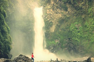 Rear view of woman standing by waterfall in forest
