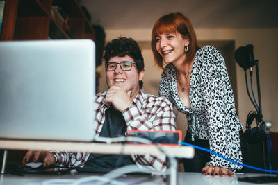 Content man in eyeglasses touching chin while interacting with female vocalist against netbook in house