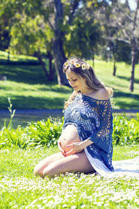 Smiling pregnant woman kneeling on grassy field