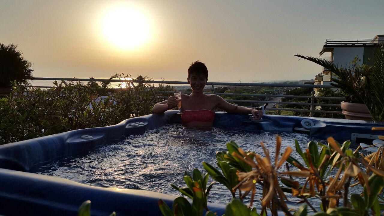 YOUNG WOMAN SITTING BY SWIMMING POOL AGAINST SKY