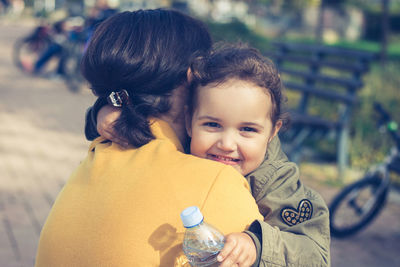 Portrait of cute smiling daughter embracing mother at park