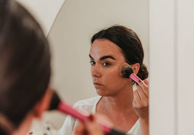 Mirror photo of beautiful young woman putting on make-up