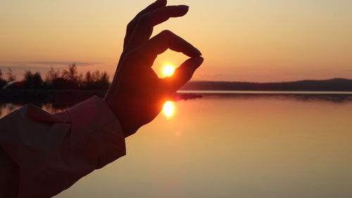 Cropped of hand gesturing against sun during sunset