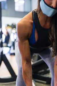 Woman in mask doing weightlifting exercises with barbell