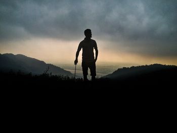 Silhouette man standing on mountain against cloudy sky during sunset