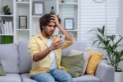Young man using phone while sitting on sofa at home