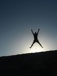 Silhouette man with arms outstretched against clear sky