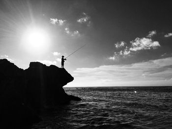 Silhouette person on rock by sea against sky