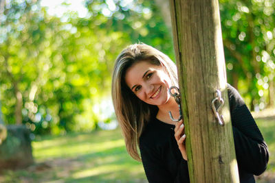 Portrait of smiling young woman standing by wooden pole