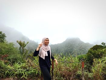 Portrait of woman showing peace sign while standing against mountain