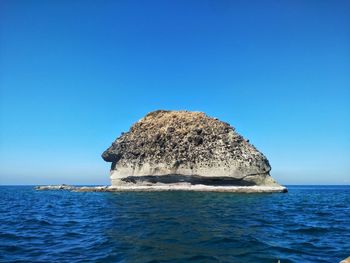 Rock formation in sea against clear blue sky