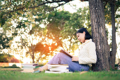 Side view of woman sitting on book against tree