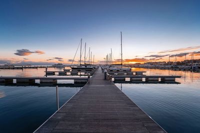 Sailboats moored at harbor against sky during sunset