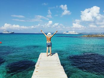 Rear view of woman standing on pier over sea against sky