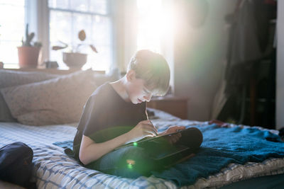 Tween sitting on bed working on laptop with touchscreen and stylus