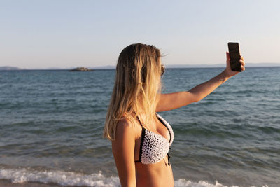 Portrait of a pretty attractive woman taking selfie. happy blonde girl next to the beach. aegean sea