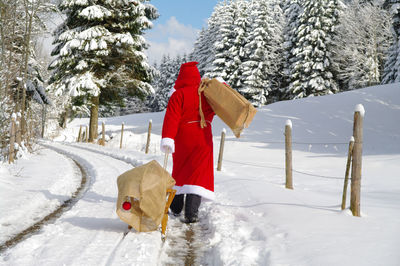Rear view of santa clause holding sled with gift on snow covered road